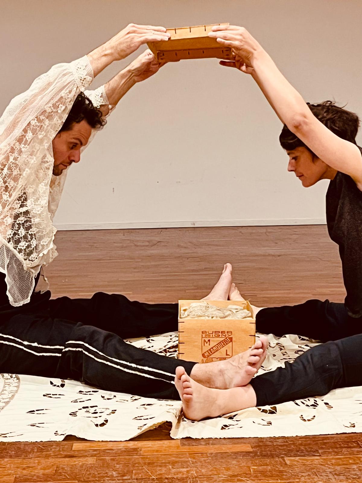 deux personnes se tenant les mains jointes au dessus de leurs tètes. Au dessous d'elles un une boite en bois remplies de dentelles