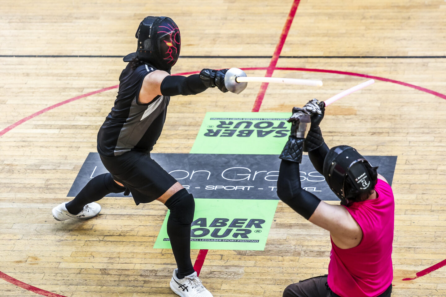 Vue en plongée sur les deux finaliste de l'Open de France de sabre laser 2025 en plein combat. Le logo Saber Tour visible au sol.