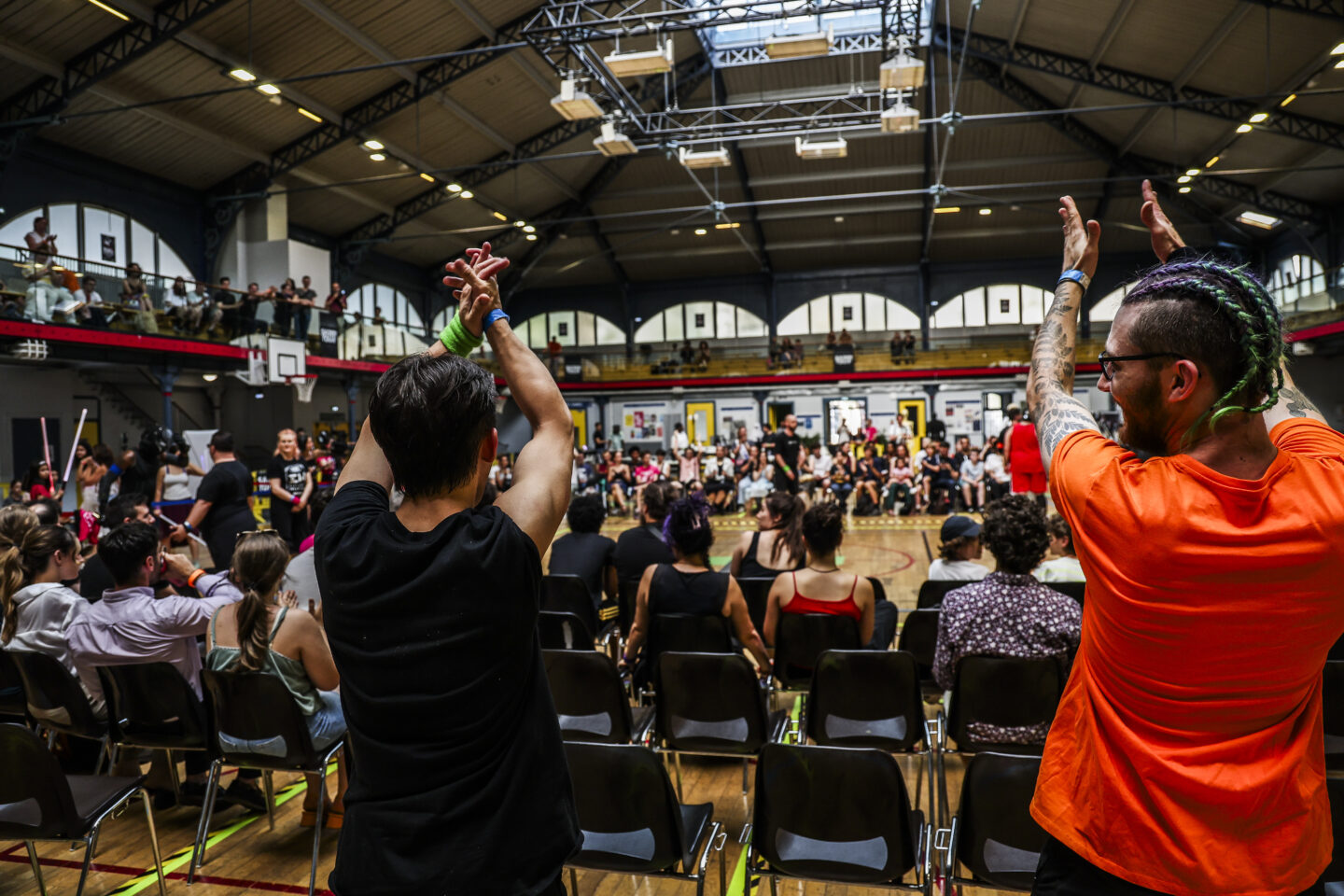 Deux spectateurs lèvent les bras en signe d'enthousiasme dans la grande salle Japy comble, lors du dernier Open de France de sabre laser sportif.